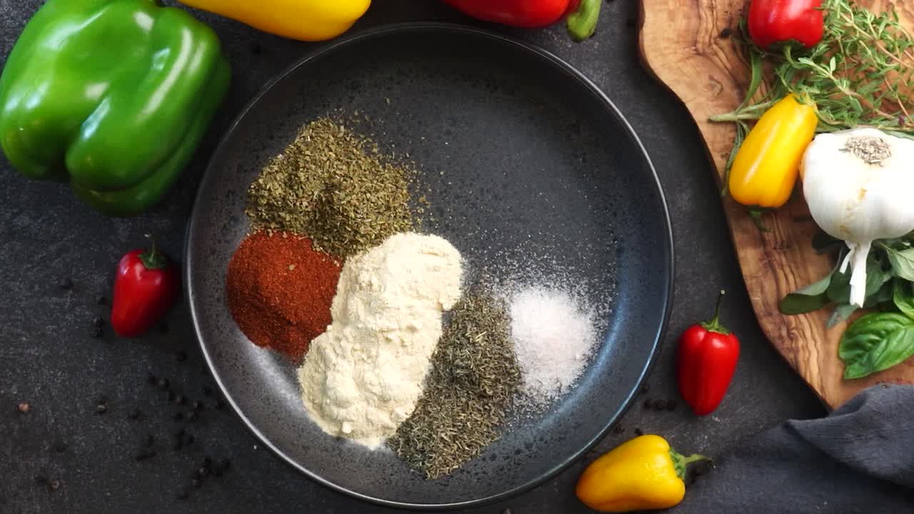 Making a vibrant Cajun Spice Blend, mixing red paprika, cayenne pepper, oregano, thyme, white garlic onion powder and black pepper in a bowl, creating a striking contrast against a black background.