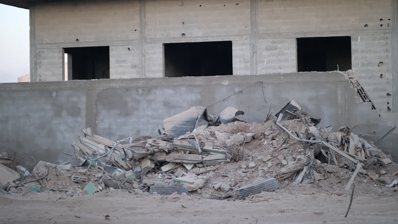 Camera pans from wall edge to show rubble and impact holes on a concrete building in Gaza.