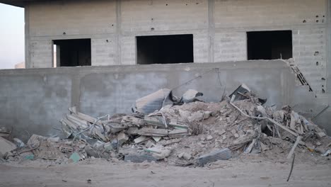 camera pans from wall edge to show rubble and impact holes on a concrete building in gaza.