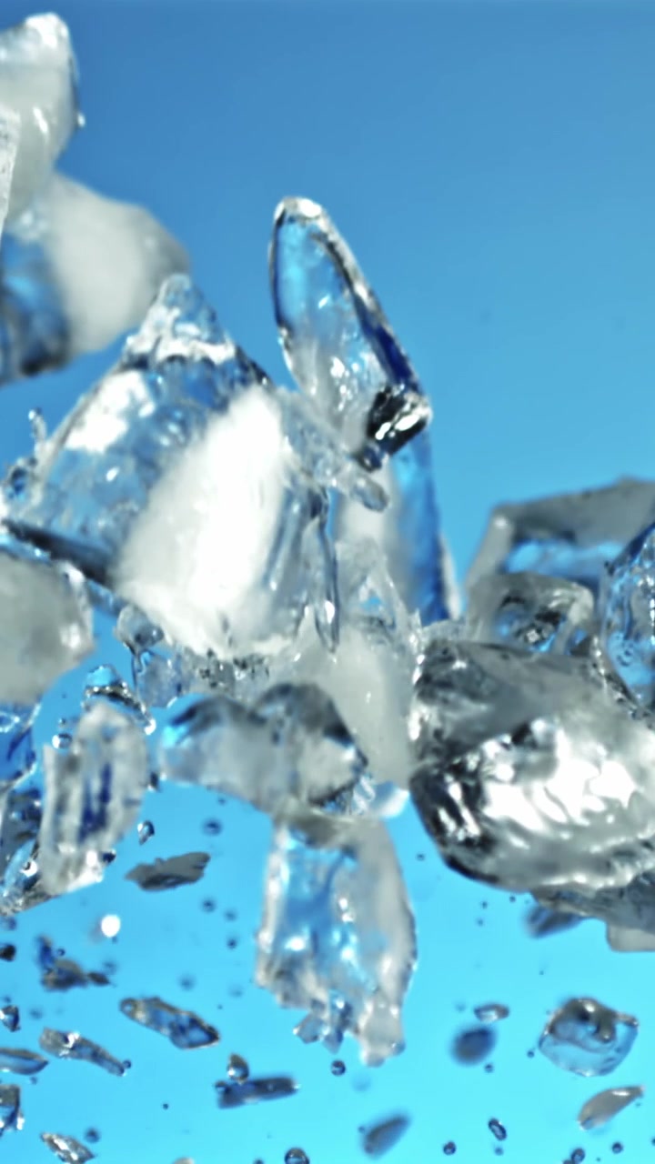 Cubetti di ghiaccio e goccioline d'acqua che salgono al rallentatore su sfondo blu