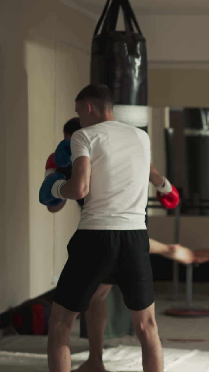 튼튼한 남자 권투 선수는 특수 장비와 권투 가방을 사용하여 적절한 권투 기법을 실행합니다. 스포츠 클럽에서 그룹 훈련 세션. 참가자에게 강사의 지침