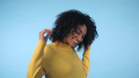 retrato de mujer negra de raza mixta con cabello rizado afro grande en fondo azul bailando y con peinado volando en el aire. 4k