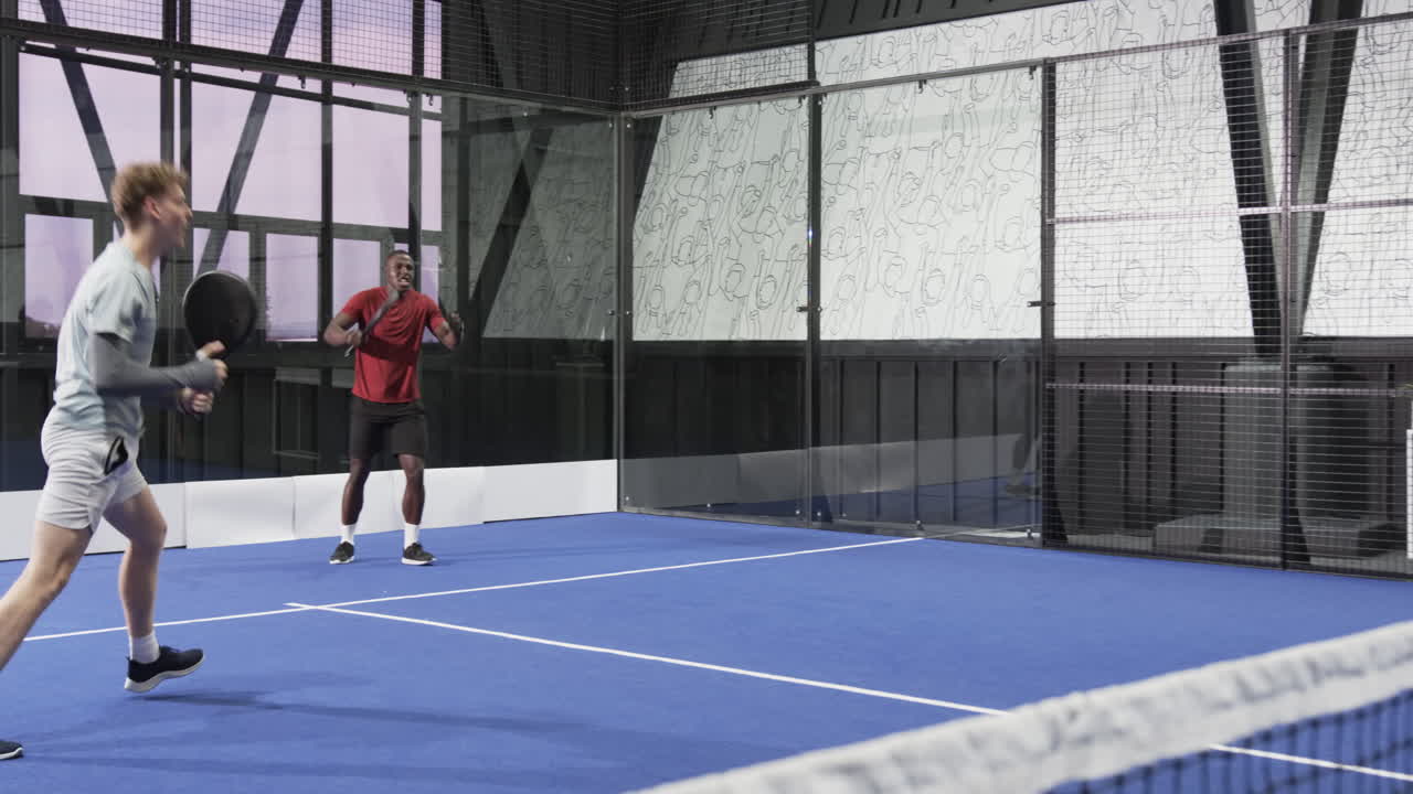 Two diverse men playing padel tennis on indoor court, focusing on intense match