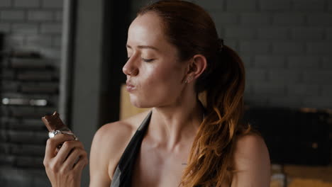 mujer comiendo una barra de proteínas en el gimnasio