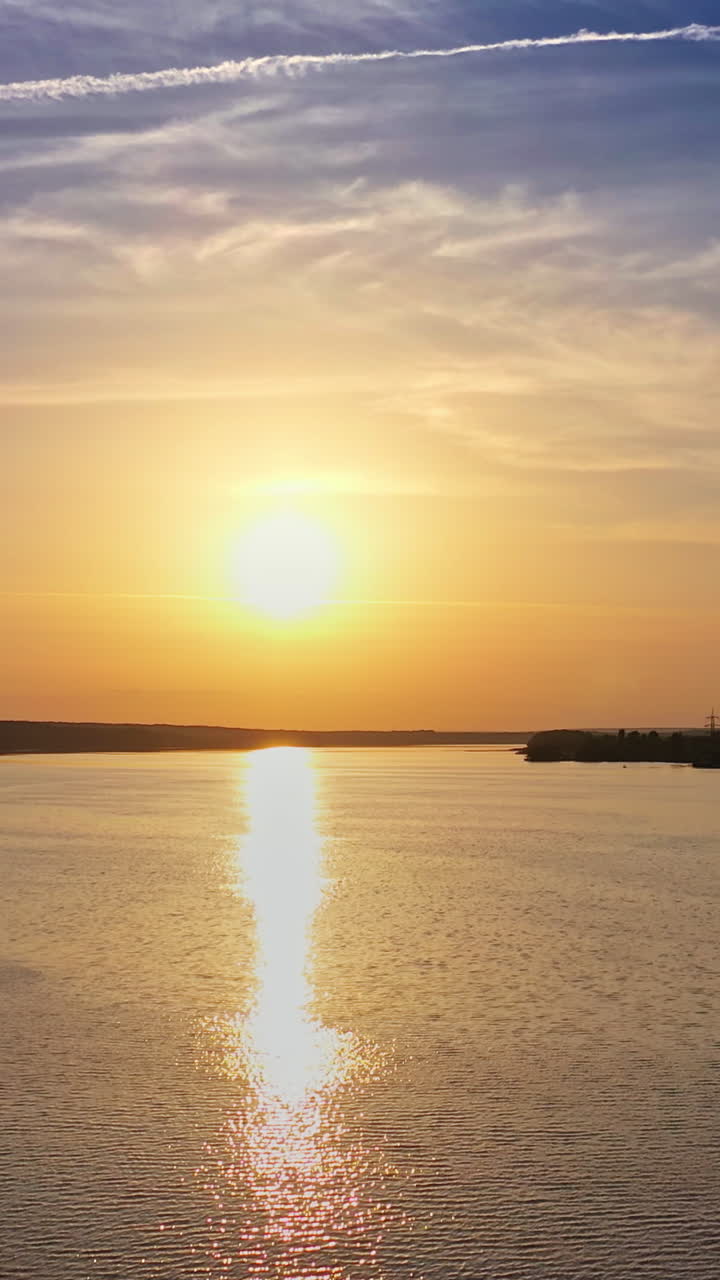 Drone landscape of sunset view on the river surface. Beautiful evening river with sun reflection. Industrial pipes with smoke from the plant near the water. Camera moves bottom up. Vertical video
