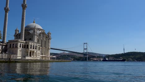 cargo ship passing under bosphorus bridge with ortakoy mosque in the foreground, istanbul, turkey