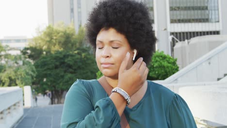 happy plus size biracial woman using smartphone and wearing earphones in city