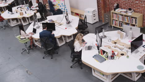 overhead time lapse of busy modern open plan office with businesspeople arriving and working at desks