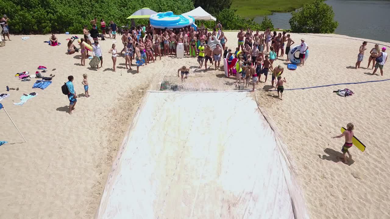 Aerial view of people enjoying a large water slide on a sandy beach