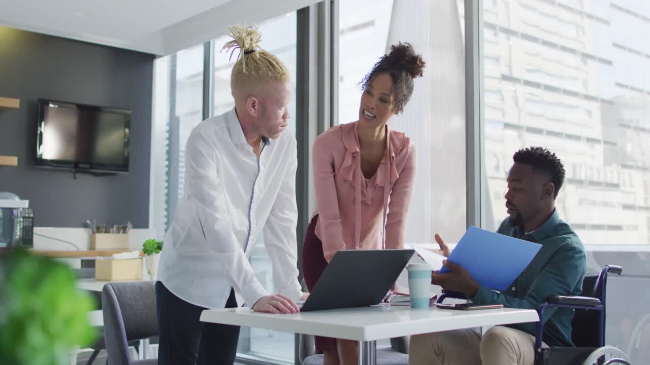 Diverse business people discussing with disabled colleague and documents in creative office