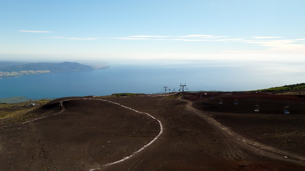 Aerial footage of Osorno Volcano in Chile, showing volcanic terrain, ski lift towers, and expansive views over Llanquihue Lake under a clear blue sky