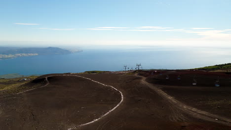 aerial footage of osorno volcano in chile, showing volcanic terrain, ski lift towers, and expansive views over llanquihue lake under a clear blue sky