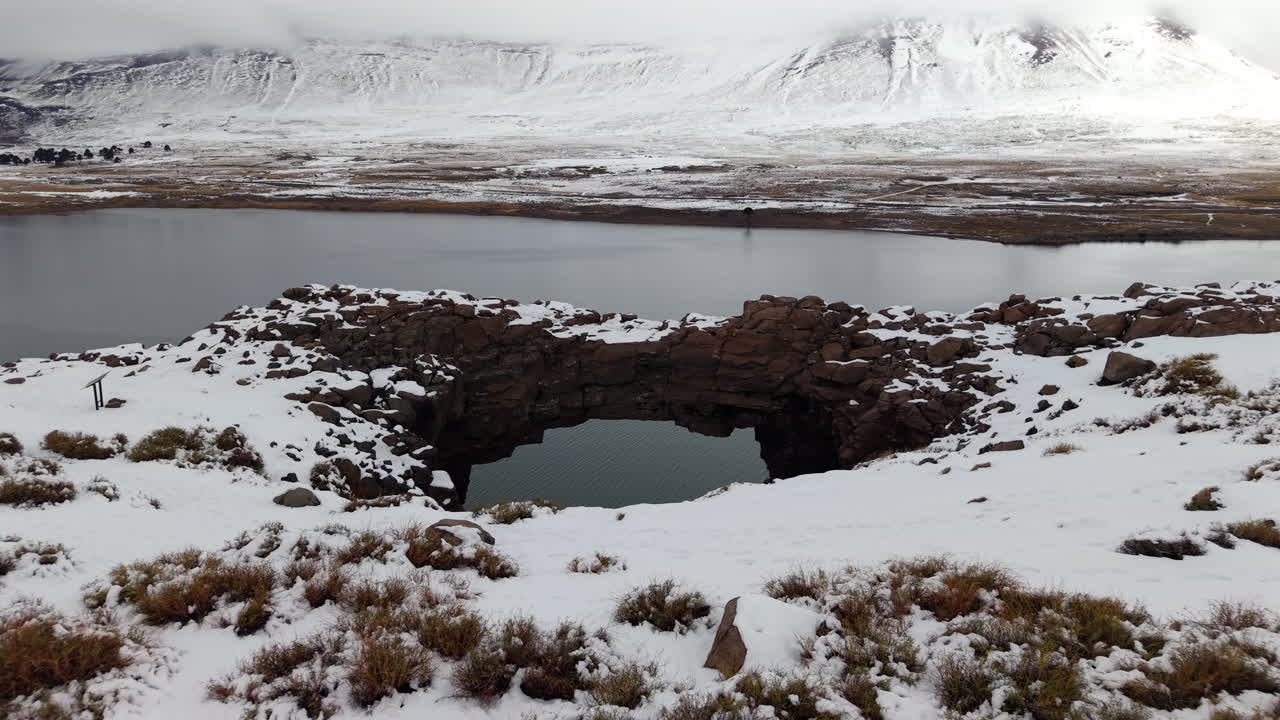 Snow-covered stone bridge crosses Caviahue lake with mountain backdrop on a peaceful winter day