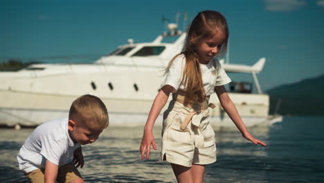 playful girl with corset to straighten back walks and boy knee-deep in sea against large yacht on sunny day. family rest on summer vacation together