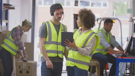 Trabajadores-Masculinos-Y-Femeninos-Que-Usan-Auriculares-En-Un-Almacén-De-Distribución-Logística-Usando-Una-Tableta-Digital