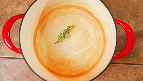 Top-down-view-of-a-hand-dropping-a-sprig-of-fresh-rosemary-into-a-pot-of-water-to-boil-rice---slow-motion