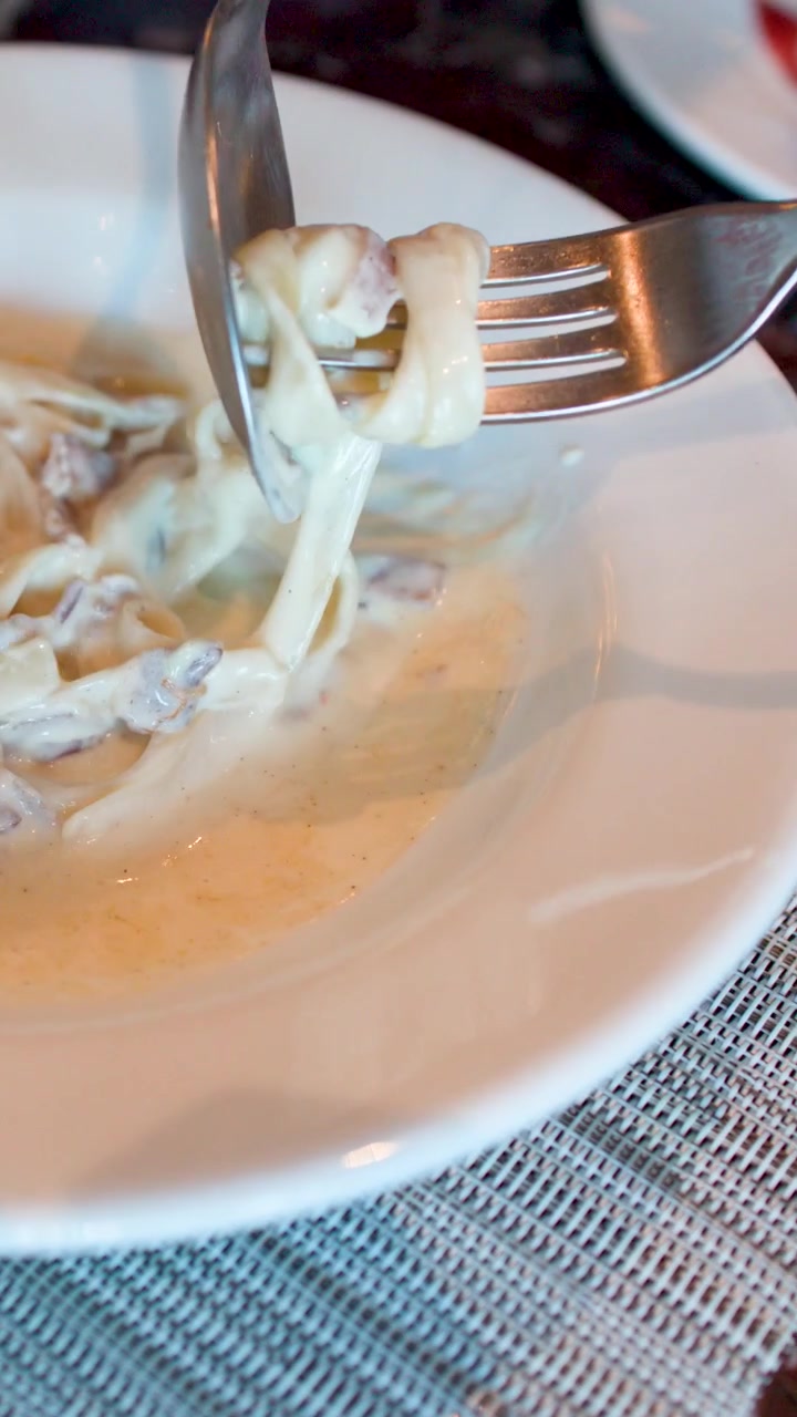 Detailní záběr na fettuccine carbonara, které se namotávají na vidličku a lžíci.
