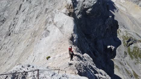 top down pan of man climbers ascending a high alpine mountain ridge. the wear backbacks, harness and helmet and walking towards steel cables. sunny day