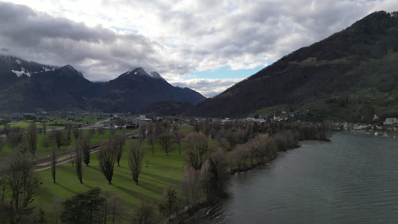 panorámica aérea a través de la costa del lago como árboles sin hojas proyectan largas sombras en los campos de hierba