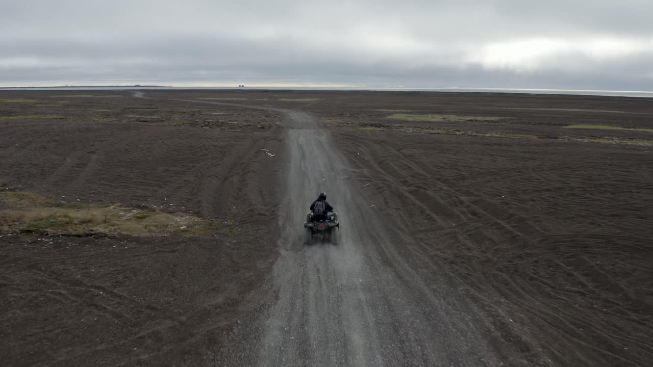 drone de seguimiento aéreo toma de un hombre solitario en un atv en la playa de arena negra en el punto más septentrional del ártico de los estados unidos cerca de barrow, alaska