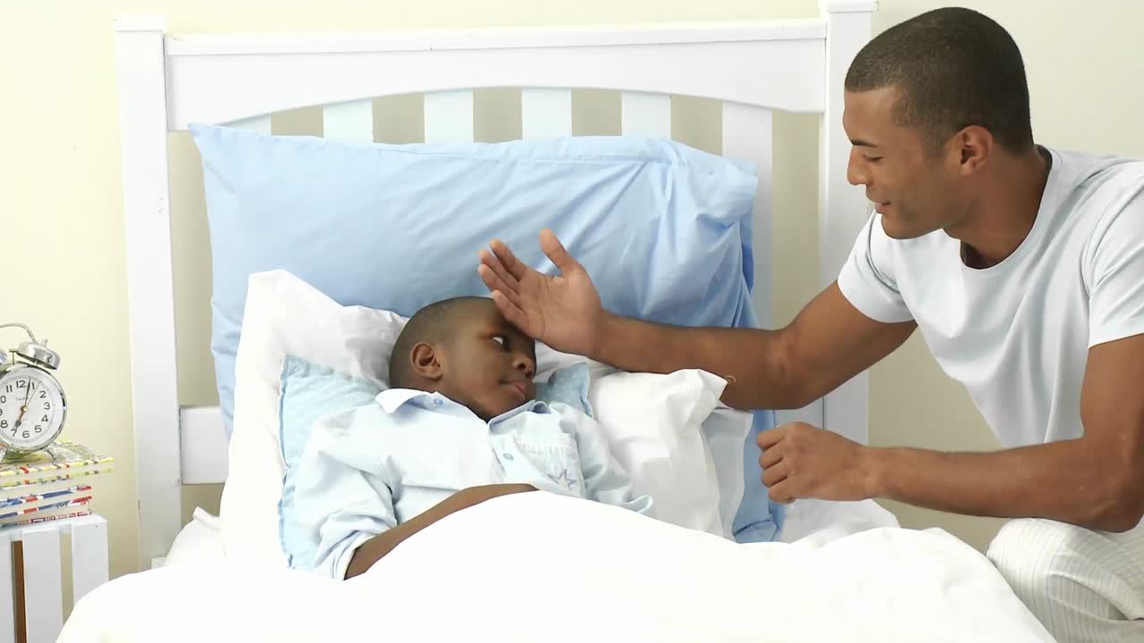 Ethnic father taking sons temperature in bedroom