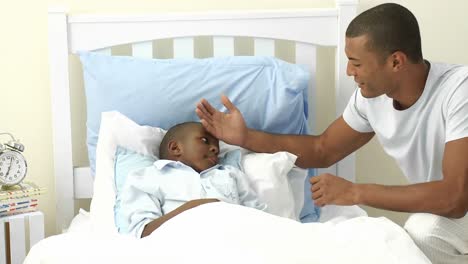 ethnic father taking sons temperature in bedroom