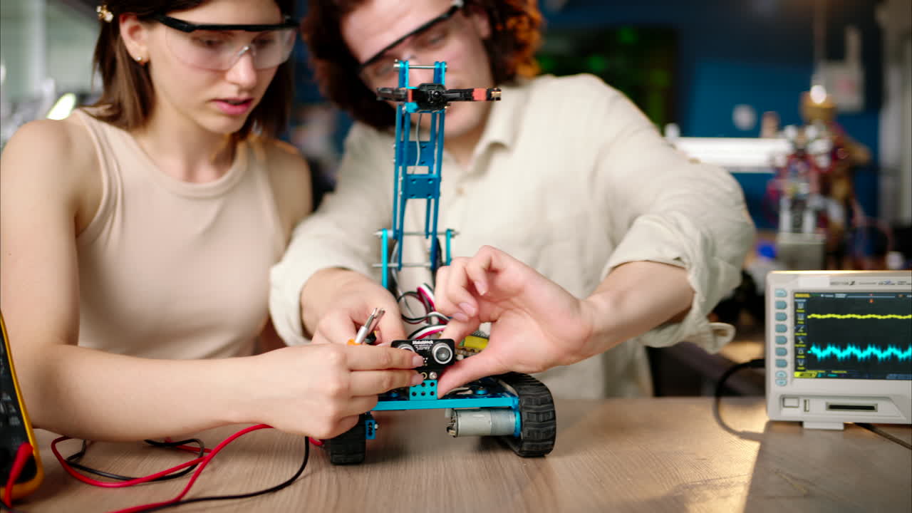 Two young happy engineers fixing a mechanical robot car in the workshop, using VR virtual reality headsets, computer programming