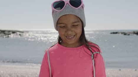 Retrato-De-Una-Niña-Hispana-Sonriendo-Tímida-En-La-Playa-Usando-Ropa-Rosa