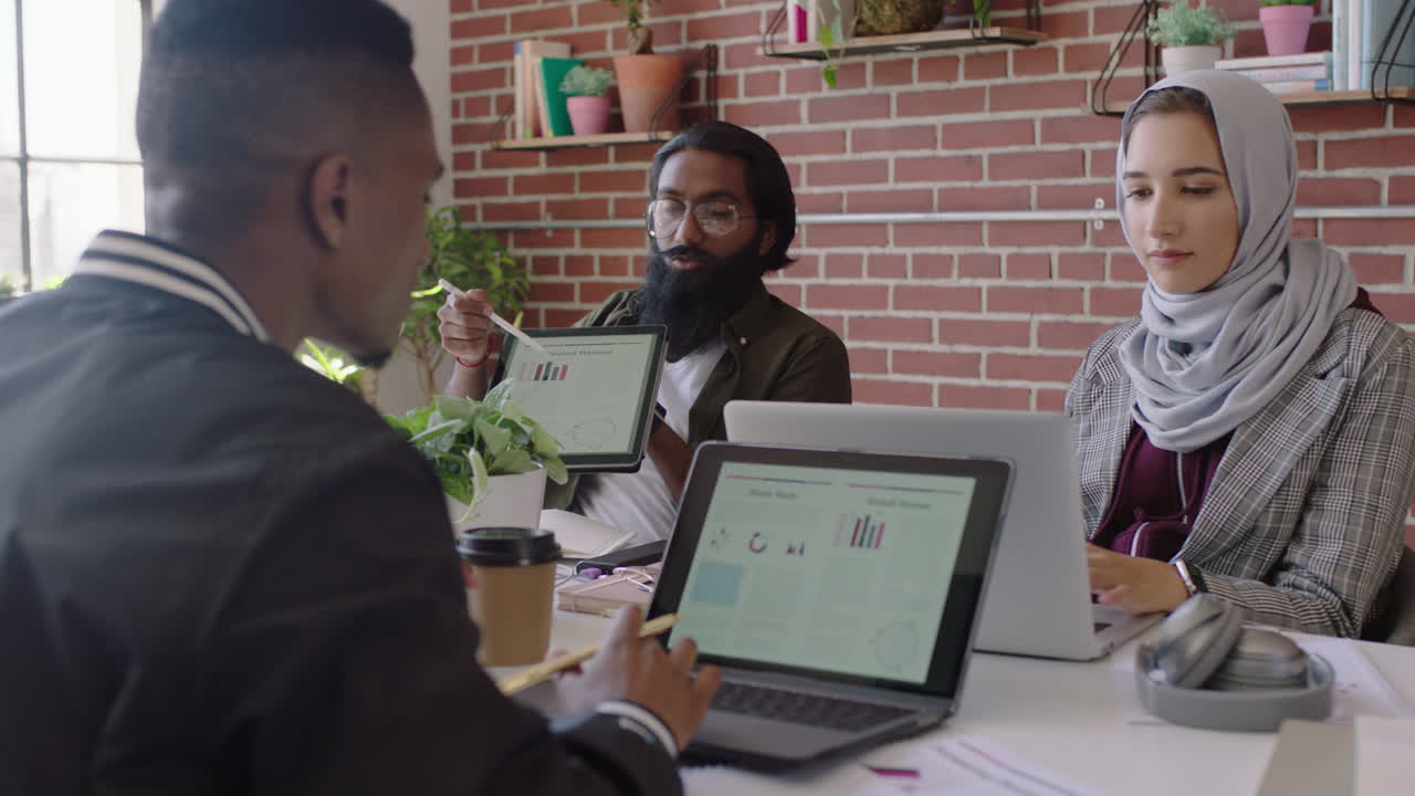 young indian businessman using tablet computer sharing creative ideas presenting project showing colleagues in office meeting diverse team working together brainstorming planning strategy
