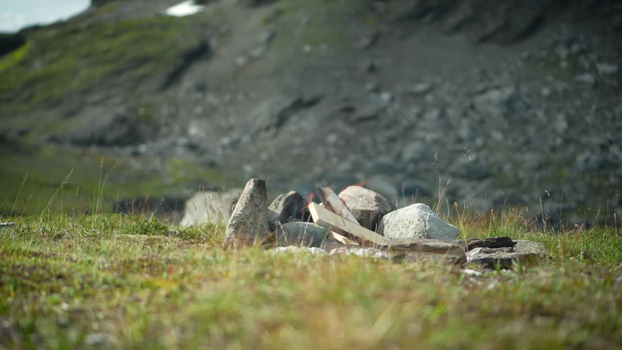 A serene, static shot of a small campfire ring in a rugged clearing near Munduk Highlands, Bali. The lush greenery and rocky terrain create a tranquil atmosphere. No people present