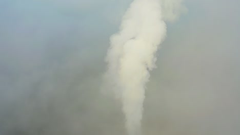 smoke from a power station chimney rising from a low, creeping fog. drone view