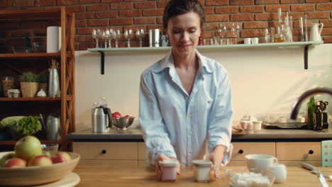 Woman-preparing-healthy-breakfast.-Girl-putting-two-yogurt-cups-on-wooden-table.