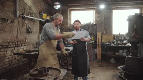 two blacksmiths discussing paper in workshop