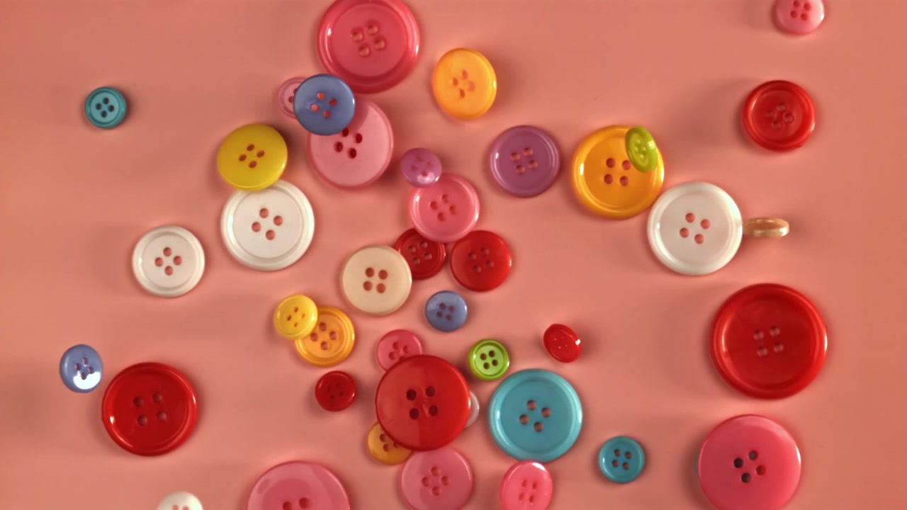 Bottoni da cucito colorati che cadono e si disperdono su uno sfondo rosa