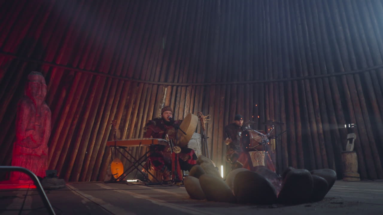 Folkemusikere spiller trommer på scene i et forsamlingshus.