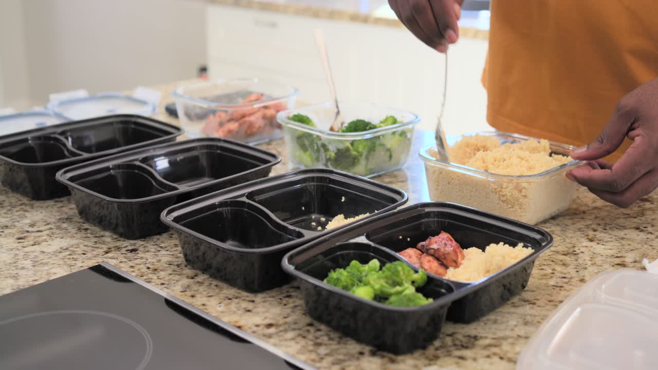 Mann mittleren Alters bereitet Behälter vor und schöpft Reis in schwarze Meal-Prep-Schalen zur Aufbewahrung, mit Textfreiraum.