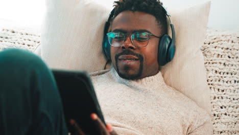 man relaxing on couch with headphones and tablet