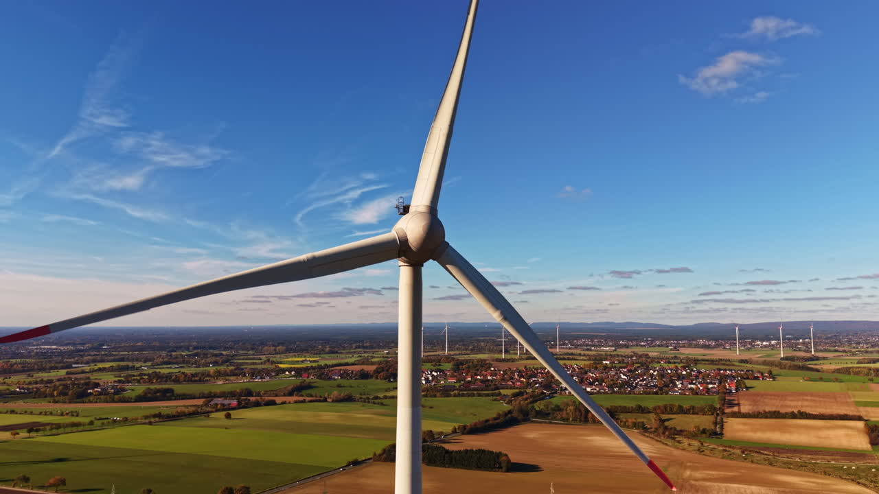 Wind turbine stands tall against clear blue skies over rolling green fields in a serene countryside landscape during late afternoon