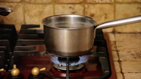 rustic kitchen scene: a cast-iron pot filled with bubbling water, steam billowing from the surface, placed over a glowing gas stove burner