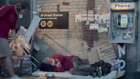 senior homeless man sleeping on sidewalk beside payphone