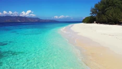 island in indonesia - beautiful coral reef under the crystal clear water, calm waves splashing on the sandy shore of the lush island with scenic mountain in the background - closeup shot