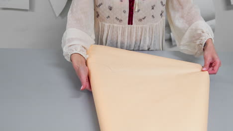 young female designer with tape-line on her neck standing in dressmaking studio and drawing lines with chalk and rule. female couturier in atelier cutting out a pattern for future clothes.