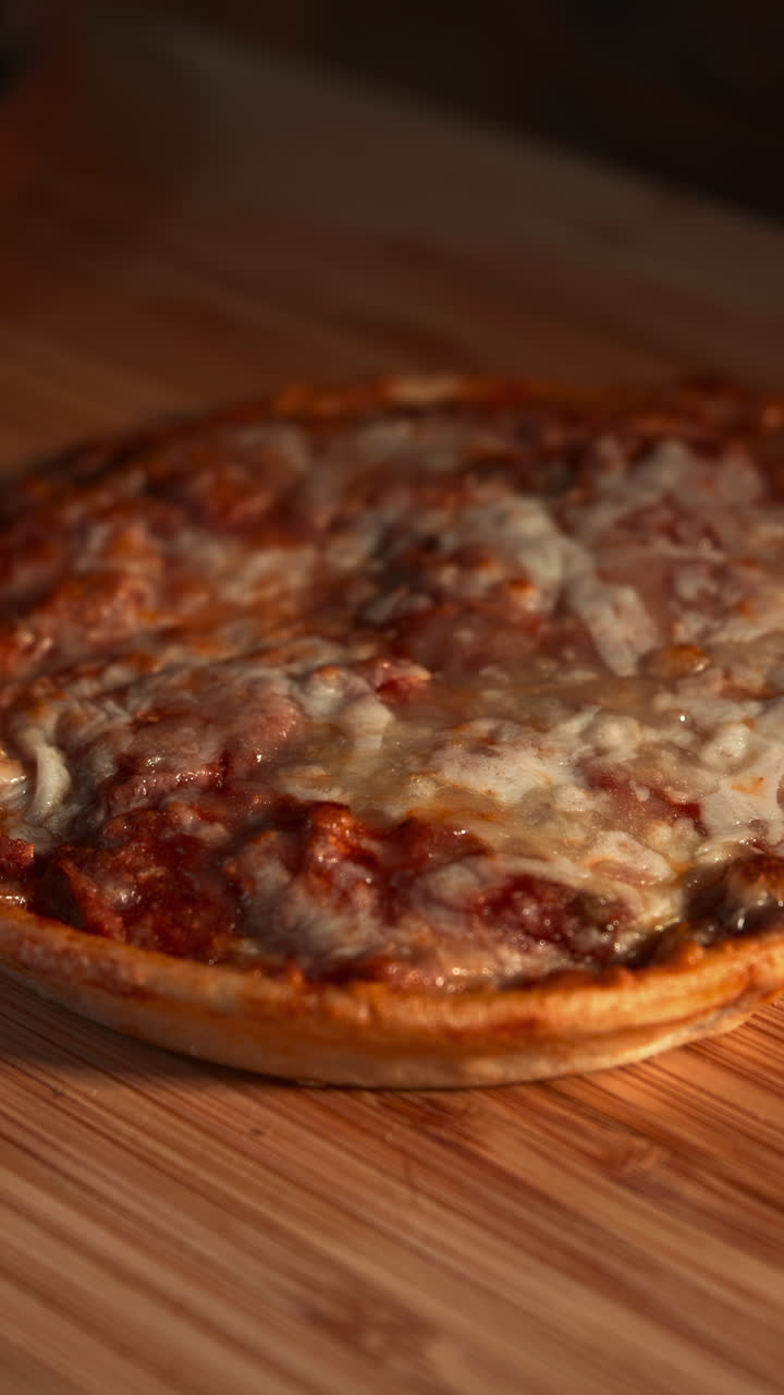 Tagliare una piccola pizza con formaggio fuso su un tagliere di legno