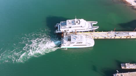 a ferry boat idles at the dock showing churned water to stern as seen from a nearly birds-eye drone view