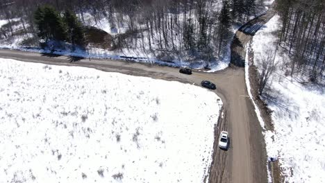 一架黑色的汽车在雪覆盖的荒野里开车并转向一条土路时,无人机拍摄了空中镜头