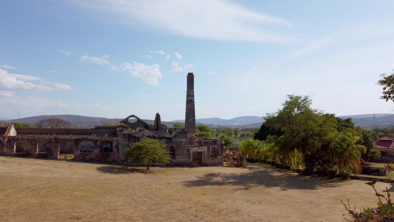 Tàn tích Hacienda Coahuixtla lịch sử với các tòa nhà đá bị bỏ hoang và ống khói cao, được bao quanh bởi phong cảnh rộng lớn dưới bầu trời xanh ở Morelos, Mexico