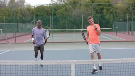 Two-diverse-male-friends-playing-doubles-celebrating-winning-point-on-outdoor-court-in-slow-motion