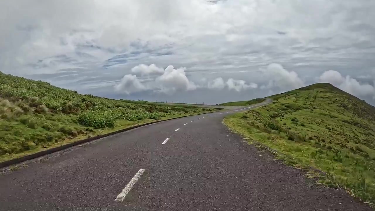 Strada rurale vuota che si snoda tra verdi colline sotto un cielo nuvoloso sull'isola di Flores.