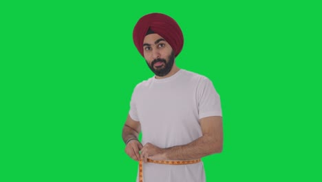 happy sikh indian man measuring waist using inch tape green screen