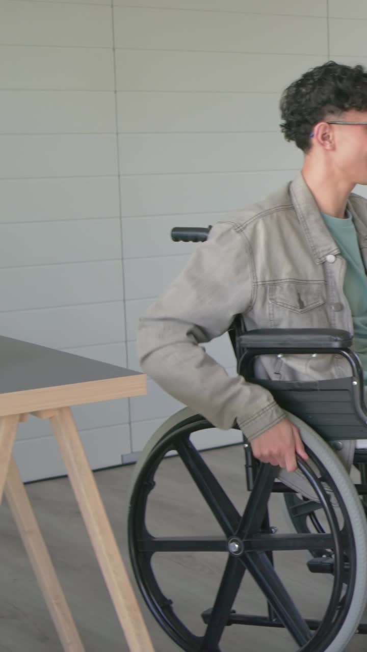 Vertical video: High-fiving man pushing wheelchair and reaching tablet at table, showing notes